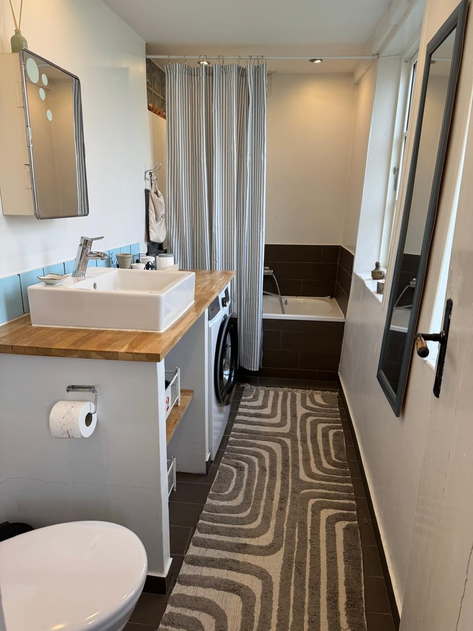 A bathroom with a wooden vanity, vessel sink and a tiled bathtub.