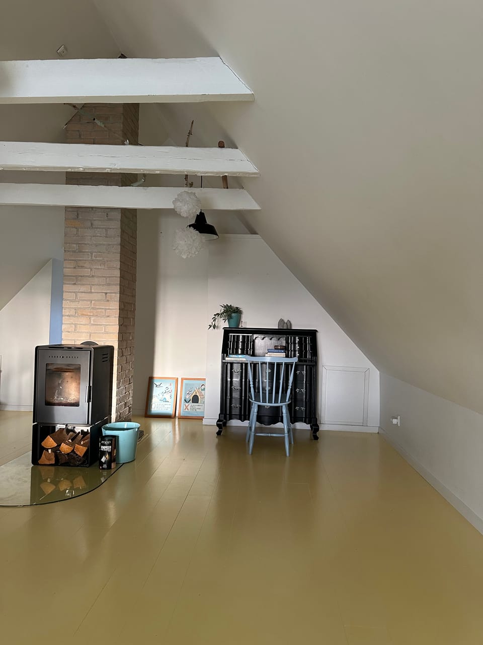 A wood-burning stove beside an exposed brick chimney and painted roof beams.