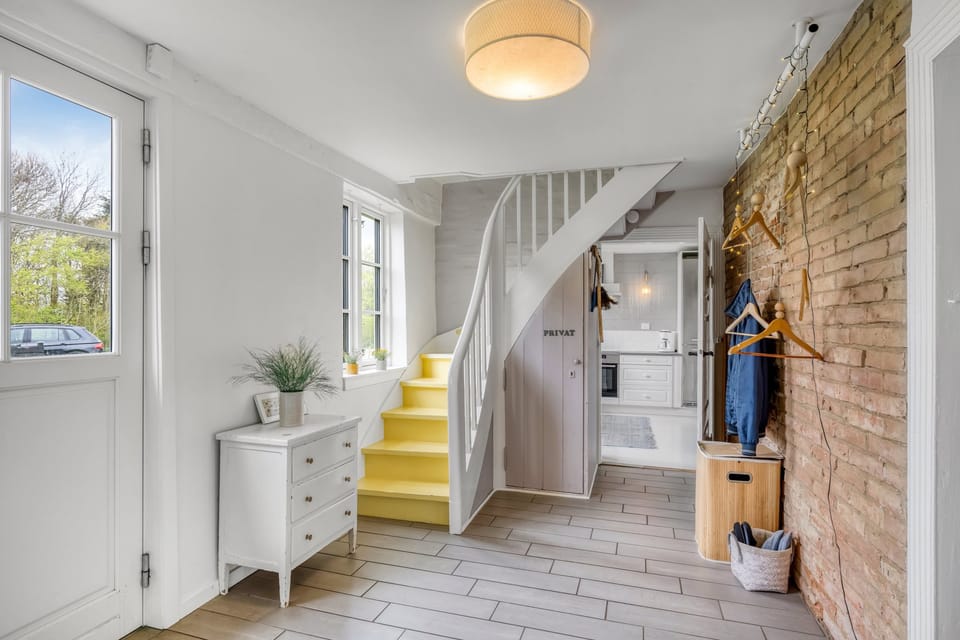 The entrance hall with a painted yellow staircase and a wall of exposed red brick.
