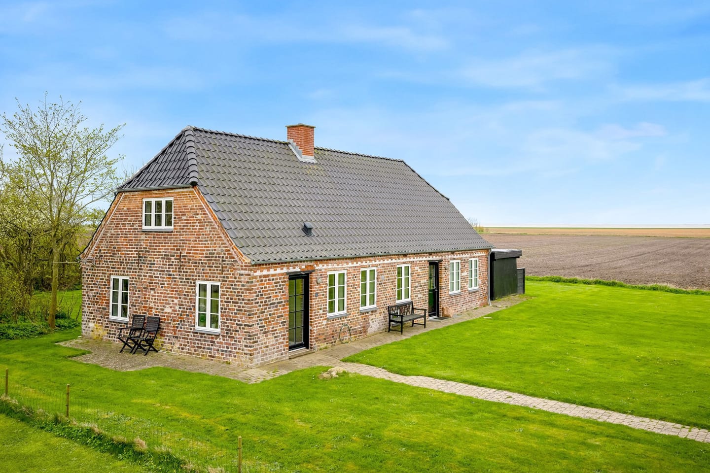 The red-brick farmhouse Villa Amada with a tiled roof, set in green marshland under a clear blue sky.