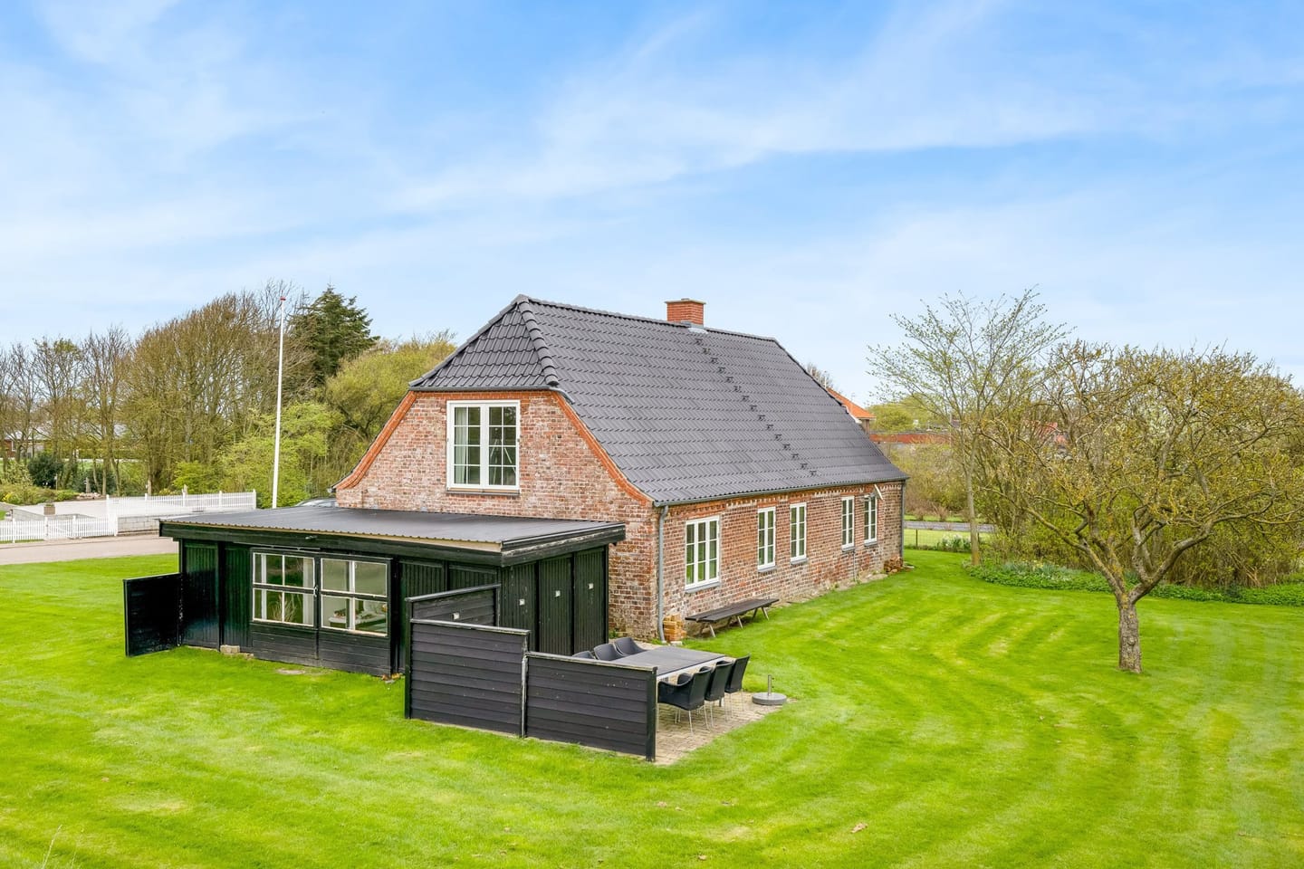 The garden side of the farmhouse, with a black conservatory, mown lawn and an apple tree.