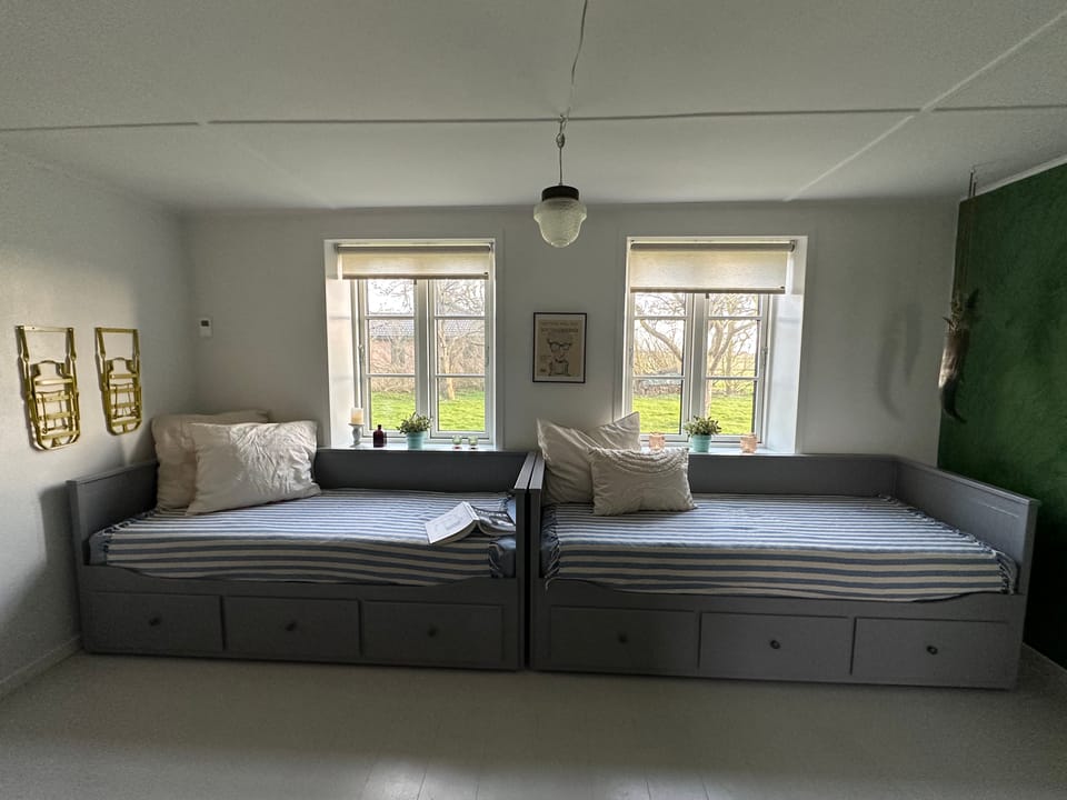 The flex room with two grey day-beds, brass sconces and windows onto the garden.