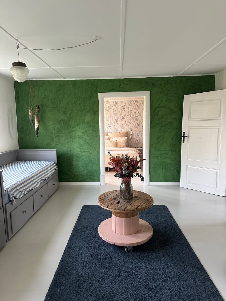 A deep marsh-green wall with a day-bed, a low table and dried flowers.
