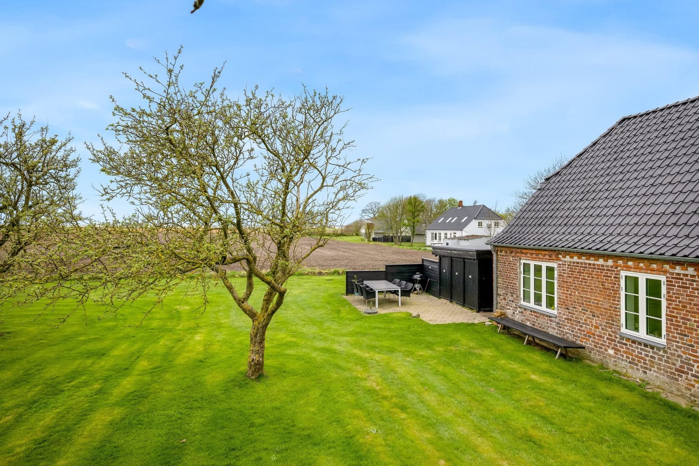 The lawn and orchard beside the house, with open fields stretching to the horizon.