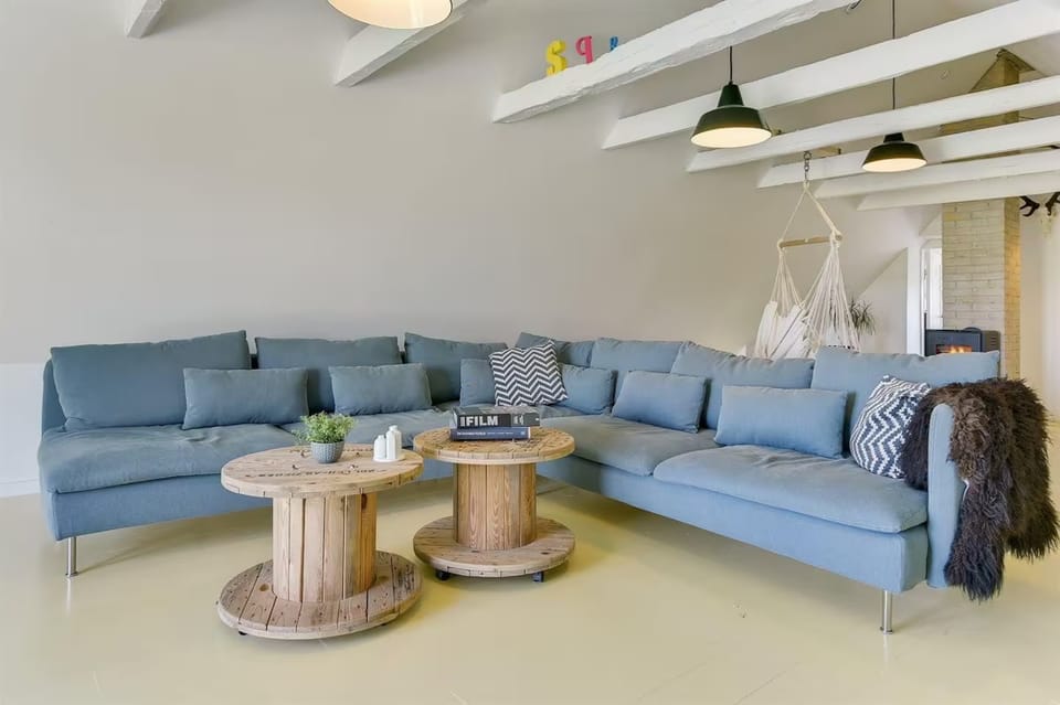 The downstairs living room with a large sofa, hanging chair and white beams.