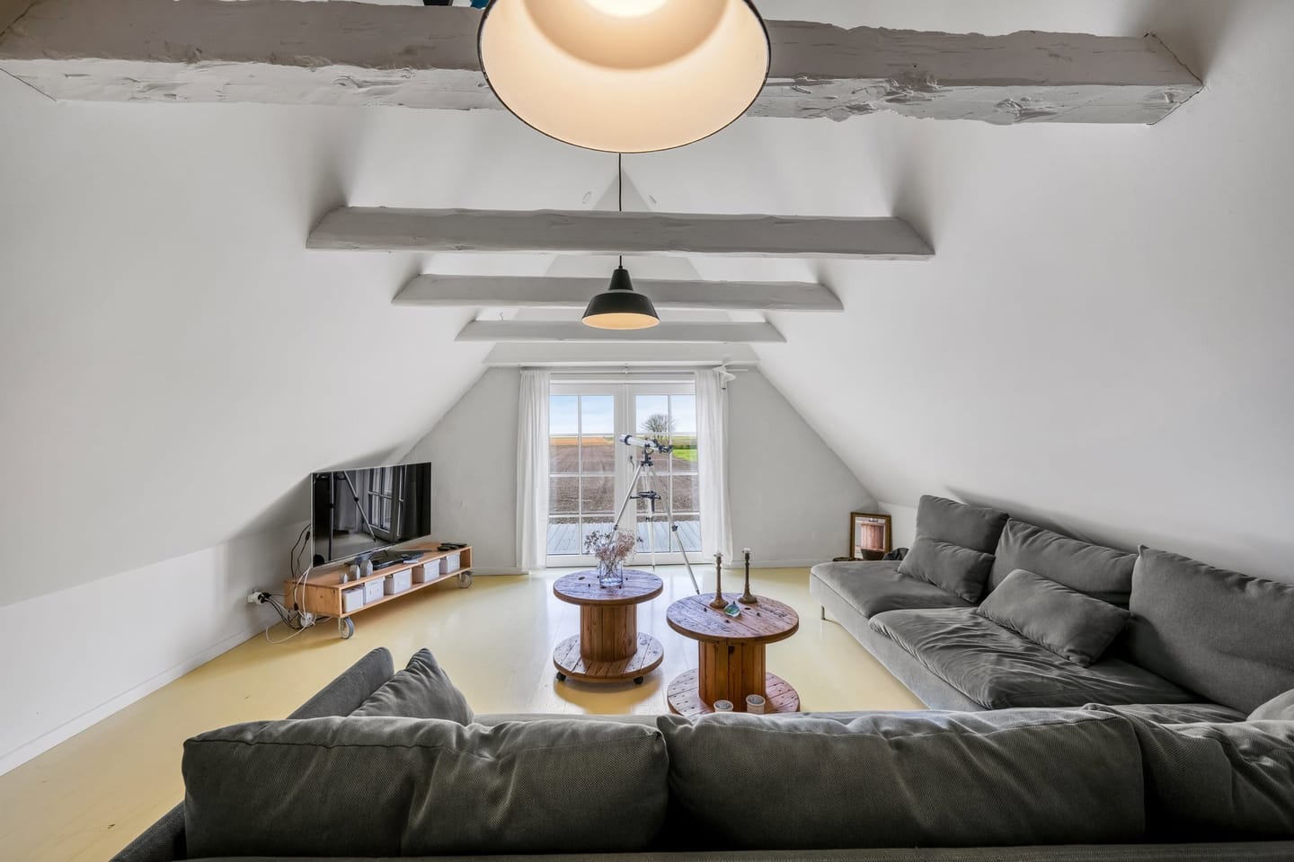 The vaulted upstairs living room with whitewashed roof beams, grey sofas and a dormer window.